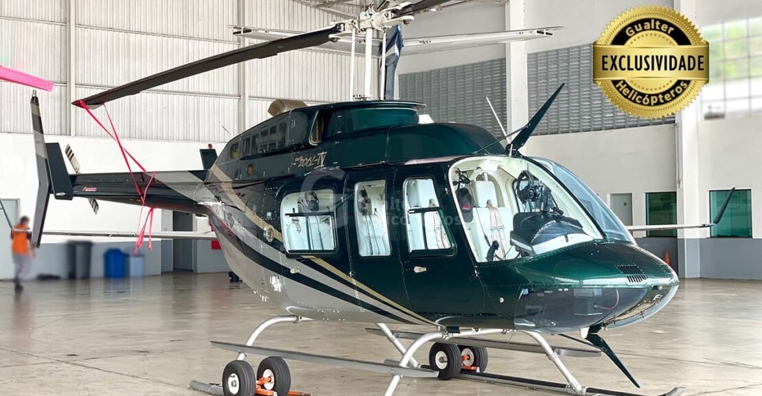 Foto lateral frente de um Bell 206L-4 verde com listras prata. Helicóptero pousado em um hangar com o selo de exclusividade na parte superior direita. Aeronave ano 1997 está à venda na Gualter Helicópteros
