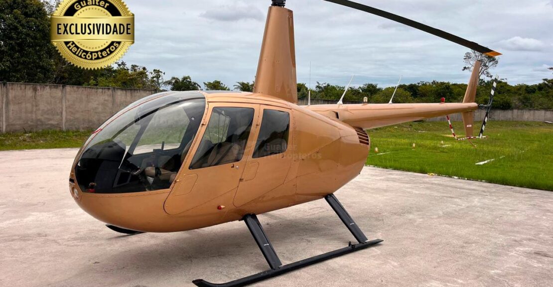 Helicóptero Robinson R44 Raven II ano 2010 dourado pousado. No canto superior esquerdo da imagem está um selo de exclusividade e, no centro da imagem, a marca d'água da empresa anunciante: Gualter Helicópteros.