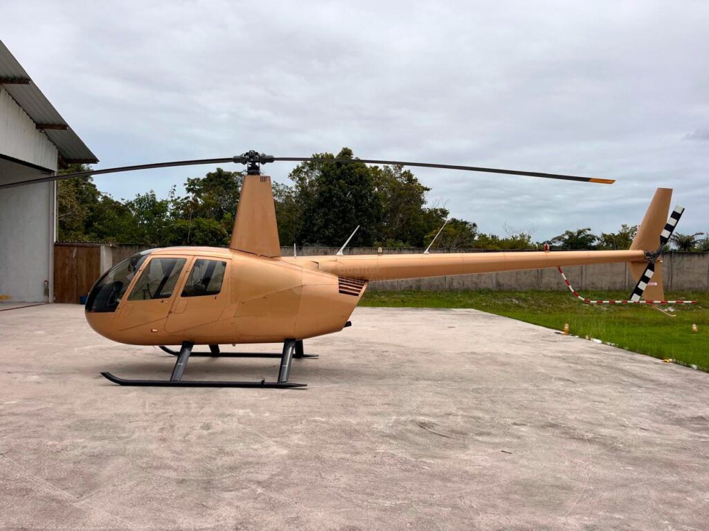 Helicóptero Robinson R44 Raven II ano 2010 dourado pousado. No centro da imagem, a marca d'água da empresa anunciante: Gualter Helicópteros.