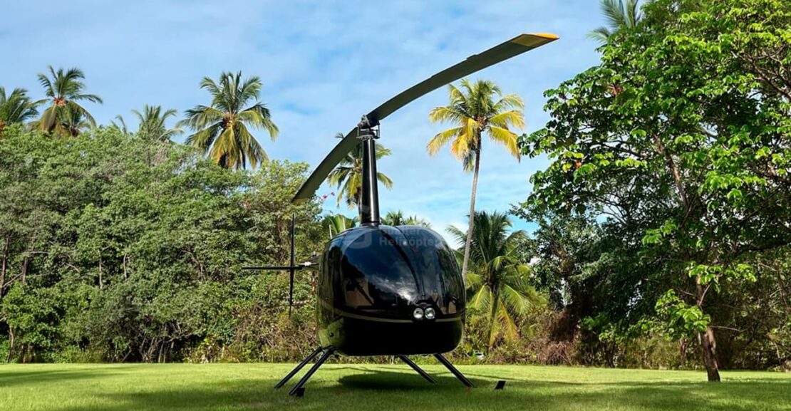 R66 Turbine preto pousado. Aeronave de frente e com paisagem verde ao fundo. Logo da Gualter Helicópteros como marca d'água no centro da imagem.