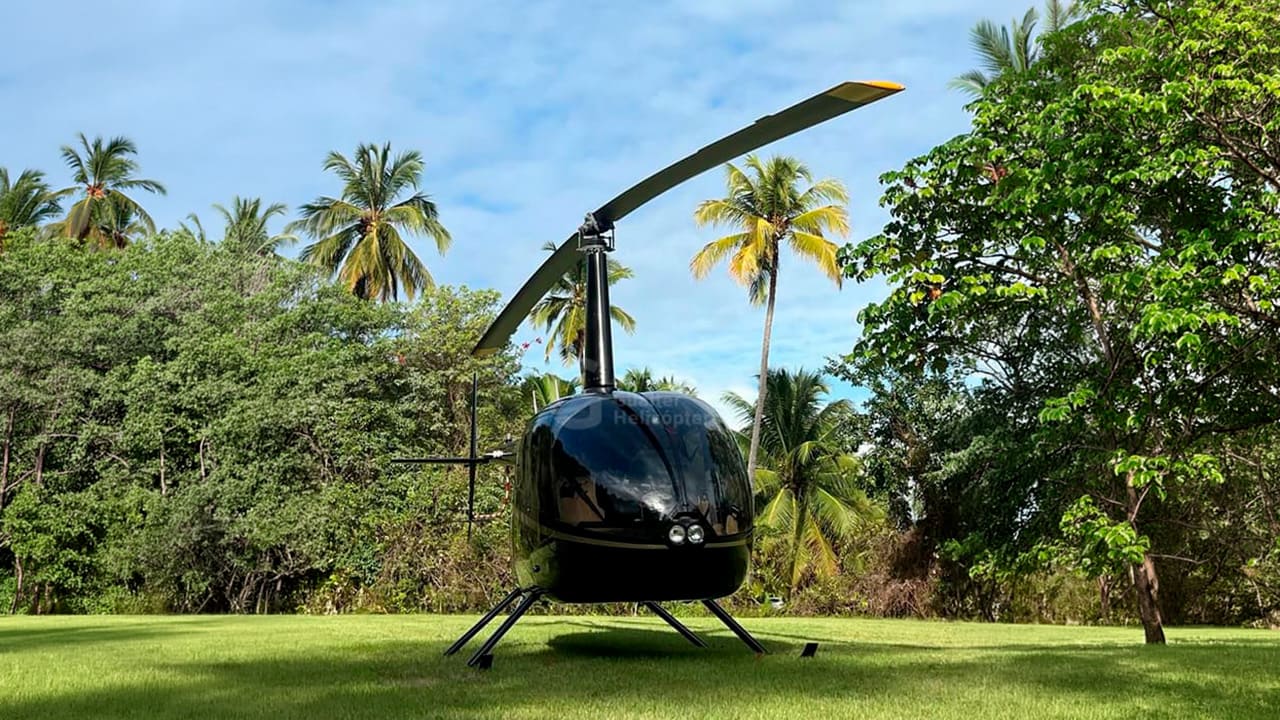 R66 Turbine preto pousado. Aeronave de frente e com paisagem verde ao fundo. Logo da Gualter Helicópteros como marca d'água no centro da imagem.